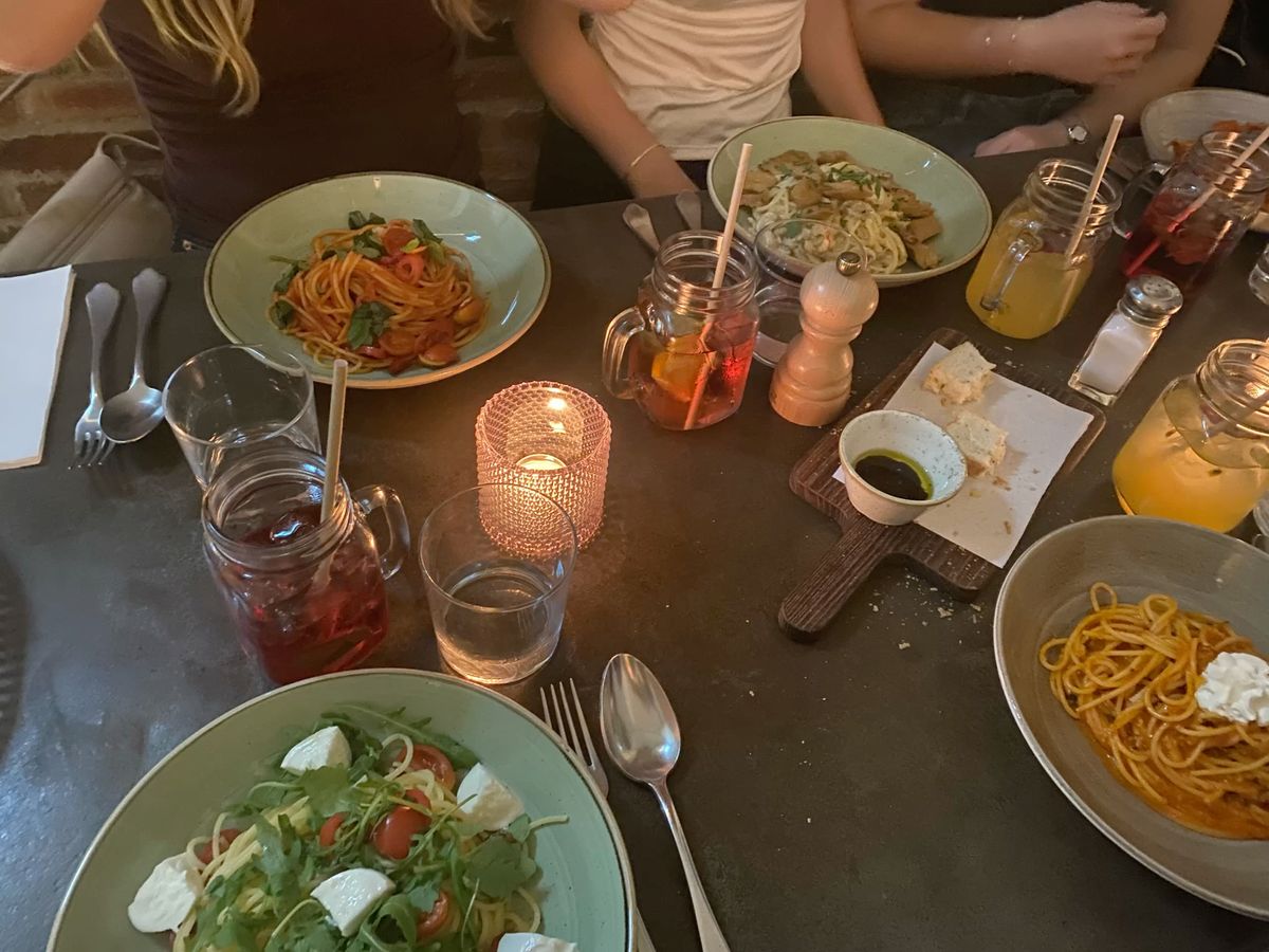 Drukke familietafel met pastagerechten en drankjes, die een ontspannen moment vastlegt dat samen wordt gedeeld tijdens een doordeweekse avondmaaltijd.